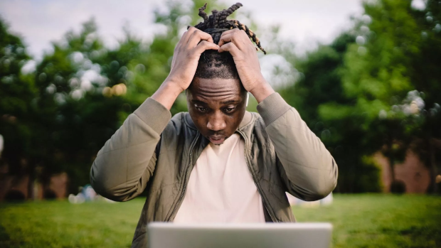 Man frustrated with his laptop puts his hands on his head